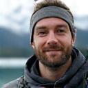 Porträt von Max aus Wien, in Outdoor-Kleidung, vor einem klaren Bergsee.